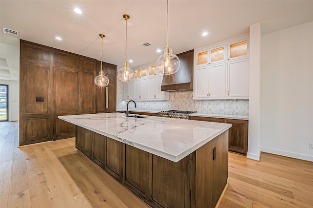 kitchen featuring a large island with sink, light stone countertops, custom range hood, and light wood-type flooring