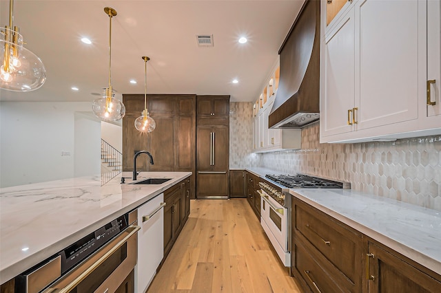 kitchen featuring wall chimney range hood, sink, hanging light fixtures, light hardwood / wood-style floors, and high end appliances