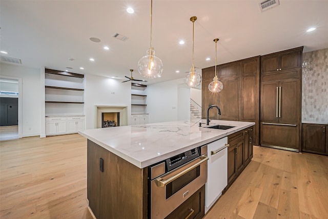 kitchen with oven, an island with sink, hanging light fixtures, sink, and light hardwood / wood-style floors