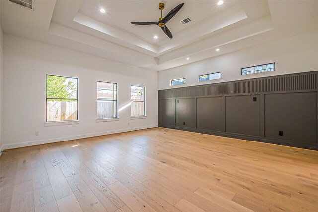 unfurnished room with visible vents, a ceiling fan, a tray ceiling, and light wood-type flooring
