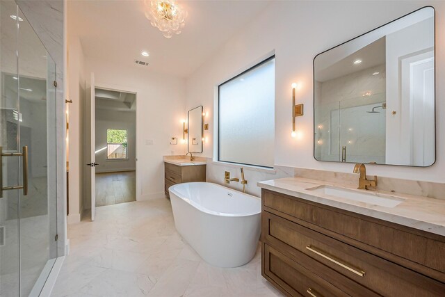 bathroom with marble finish floor, a freestanding tub, two vanities, a shower stall, and a sink