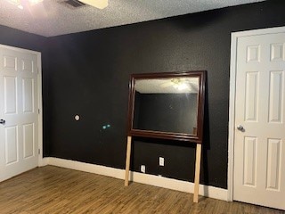 unfurnished bedroom with dark wood-type flooring, a textured ceiling, and ceiling fan