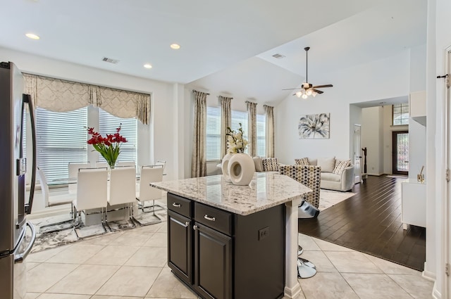 kitchen with light hardwood / wood-style flooring, a kitchen island, ceiling fan, stainless steel refrigerator, and a breakfast bar