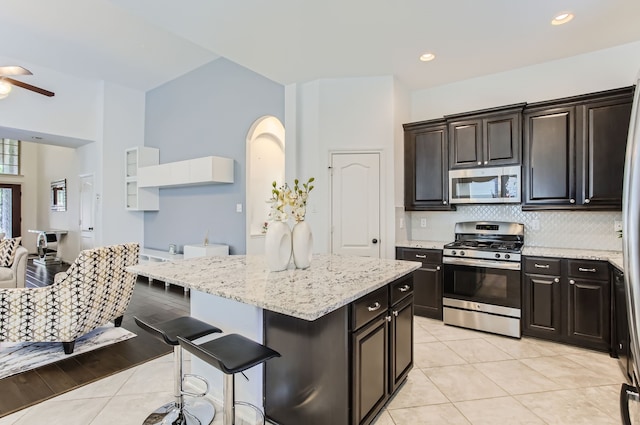 kitchen featuring a kitchen island, light hardwood / wood-style floors, stainless steel appliances, light stone counters, and a breakfast bar