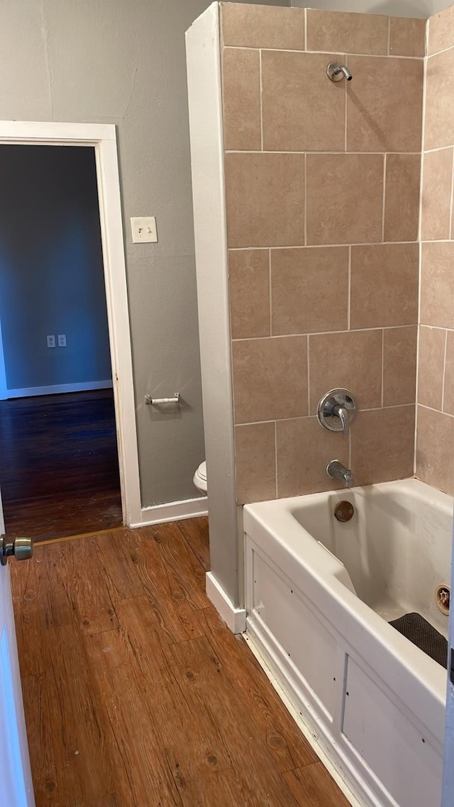 bathroom with toilet, tiled shower / bath combo, and wood-type flooring