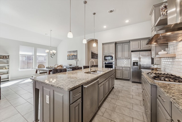 kitchen featuring sink, backsplash, stainless steel appliances, wall chimney exhaust hood, and a kitchen island with sink