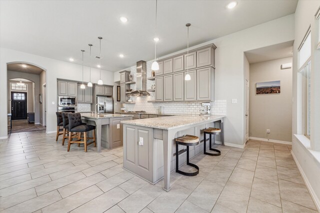 kitchen with wall chimney exhaust hood, kitchen peninsula, pendant lighting, and a breakfast bar area