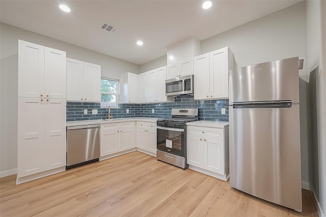 kitchen with tasteful backsplash, sink, white cabinetry, light hardwood / wood-style floors, and stainless steel appliances