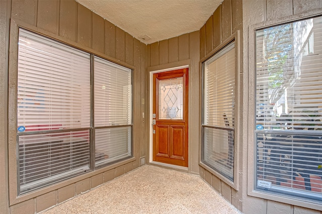 doorway to outside featuring a textured ceiling and wood walls