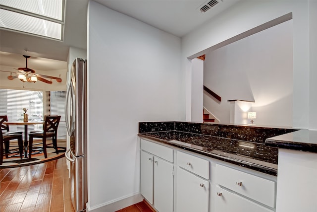 kitchen with light hardwood / wood-style floors, white cabinets, dark stone countertops, and stainless steel fridge