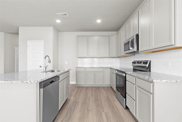 kitchen featuring decorative backsplash, appliances with stainless steel finishes, light wood-type flooring, light stone counters, and sink