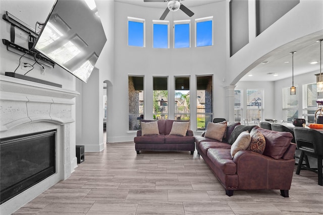 living room with ornate columns, light wood-type flooring, a high ceiling, and ceiling fan