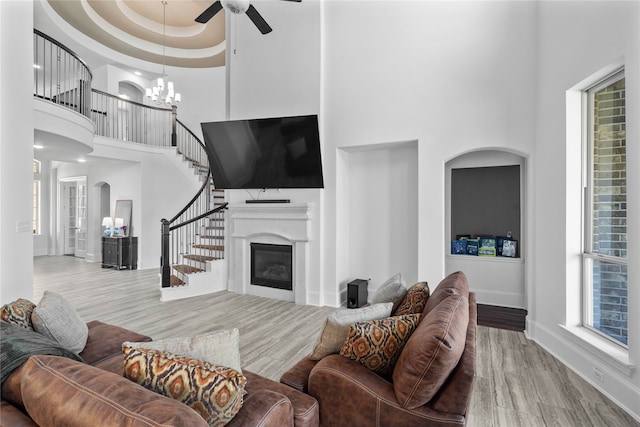 living room with a high ceiling, ceiling fan with notable chandelier, a tray ceiling, and light hardwood / wood-style floors