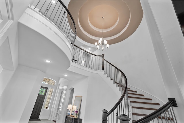 staircase featuring a raised ceiling, a towering ceiling, and a chandelier