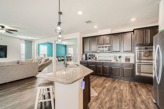 kitchen with a breakfast bar area, dark wood-type flooring, an island with sink, stainless steel appliances, and sink