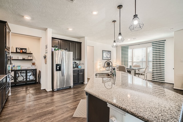 kitchen featuring sink, dark hardwood / wood-style flooring, hanging light fixtures, stainless steel fridge, and a kitchen island with sink