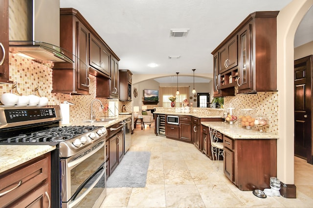 kitchen featuring wall chimney range hood, appliances with stainless steel finishes, pendant lighting, and decorative backsplash