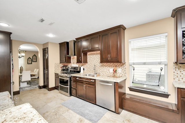 kitchen with wall chimney range hood, backsplash, appliances with stainless steel finishes, and sink