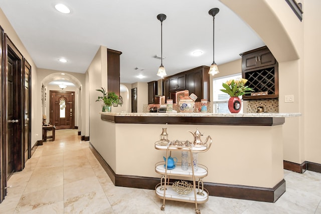 kitchen featuring kitchen peninsula, dark brown cabinetry, decorative light fixtures, light stone counters, and decorative backsplash