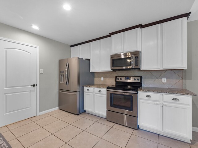 kitchen with stainless steel appliances, backsplash, dark stone countertops, light tile patterned floors, and white cabinetry