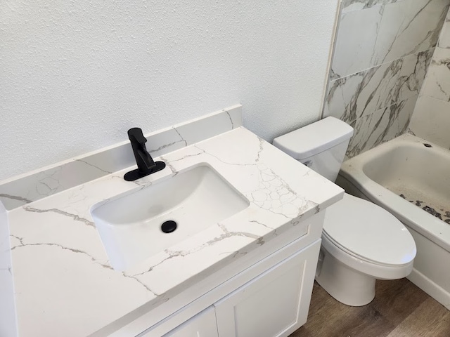 bathroom with vanity, toilet, a tub to relax in, and wood-type flooring