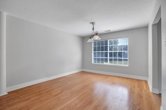 empty room with a textured ceiling and light hardwood / wood-style flooring