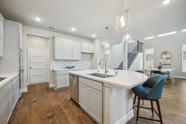 kitchen featuring white cabinets, an island with sink, stainless steel dishwasher, dark wood-type flooring, and sink