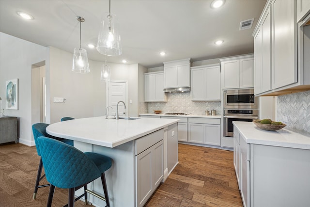 kitchen featuring dark hardwood / wood-style floors, a center island with sink, sink, white cabinetry, and appliances with stainless steel finishes