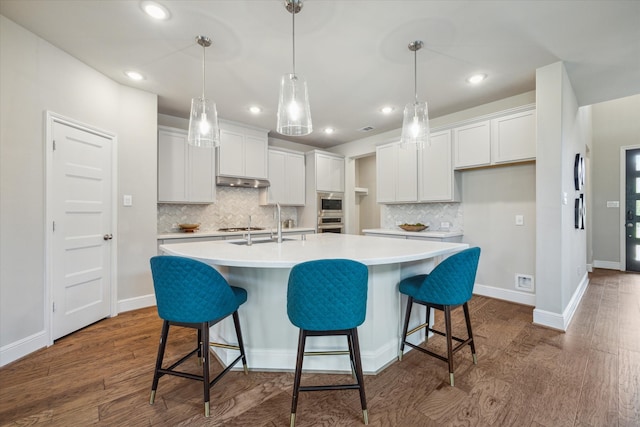 kitchen with white cabinetry, dark wood-type flooring, backsplash, and an island with sink