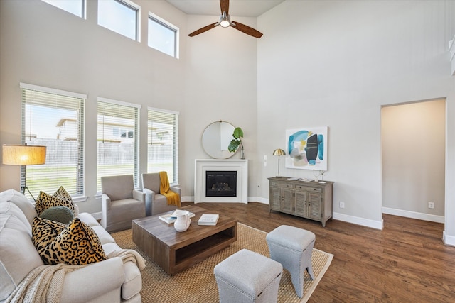 living room featuring a high ceiling, ceiling fan, a healthy amount of sunlight, and dark hardwood / wood-style flooring