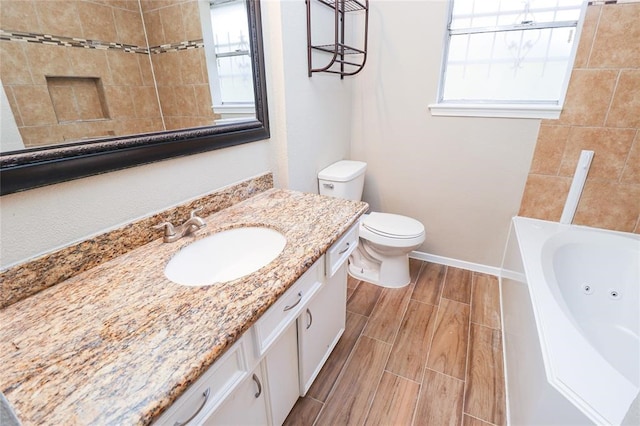 bathroom featuring a bath, toilet, a healthy amount of sunlight, and vanity