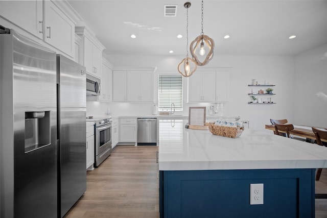 kitchen with a kitchen island, stainless steel appliances, decorative light fixtures, light wood-type flooring, and white cabinets