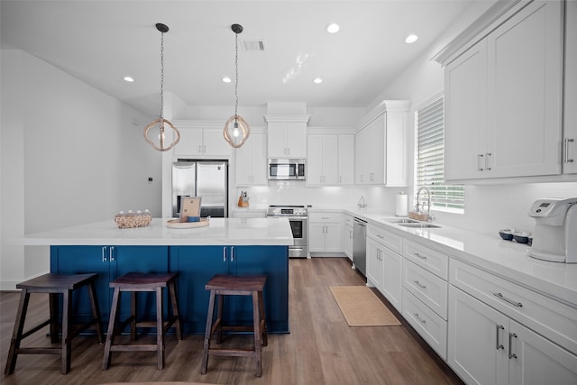 kitchen with sink, a center island, stainless steel appliances, decorative light fixtures, and white cabinets