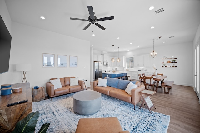 living room featuring ceiling fan with notable chandelier and light wood-type flooring