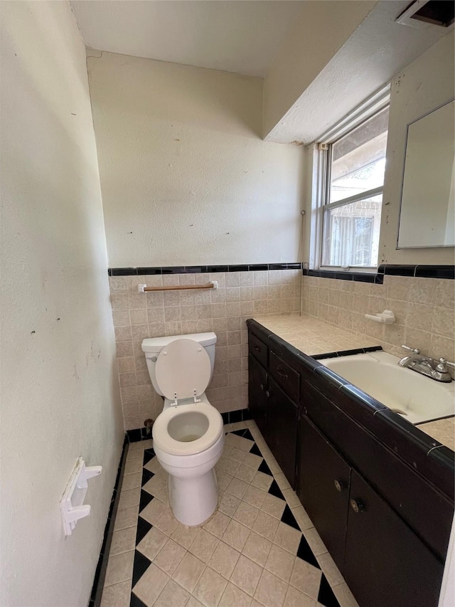 bathroom with tile patterned floors, vanity, tile walls, and toilet