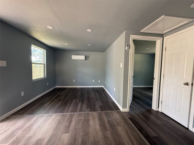 spare room with dark wood-type flooring, a textured ceiling, and a wall unit AC