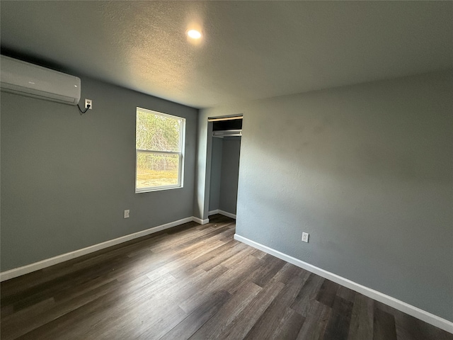 unfurnished bedroom with an AC wall unit, a textured ceiling, hardwood / wood-style flooring, and a closet