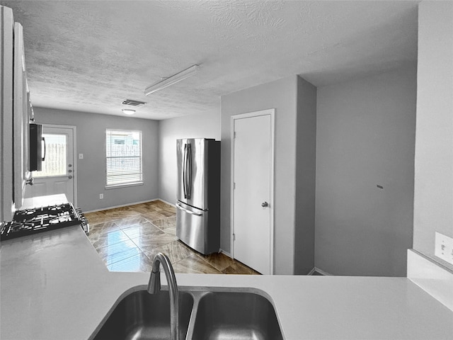 kitchen with a textured ceiling, stove, sink, and stainless steel refrigerator