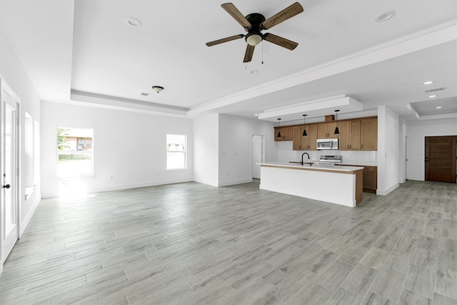 unfurnished living room with a tray ceiling, a healthy amount of sunlight, and light hardwood / wood-style flooring