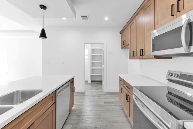 kitchen with light wood-type flooring, appliances with stainless steel finishes, and decorative light fixtures