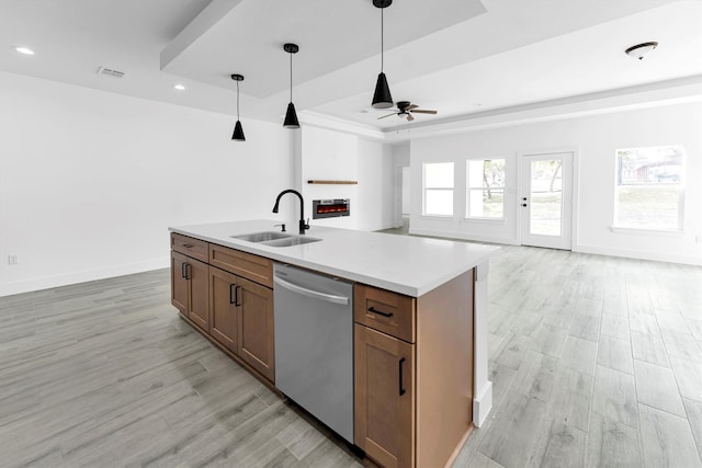 kitchen featuring decorative light fixtures, sink, an island with sink, dishwasher, and light hardwood / wood-style flooring