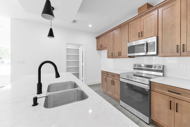 kitchen with stainless steel appliances, decorative light fixtures, light stone countertops, sink, and light hardwood / wood-style floors