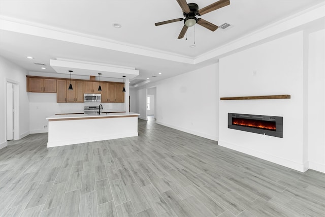 unfurnished living room featuring light wood-type flooring, a raised ceiling, sink, and ceiling fan