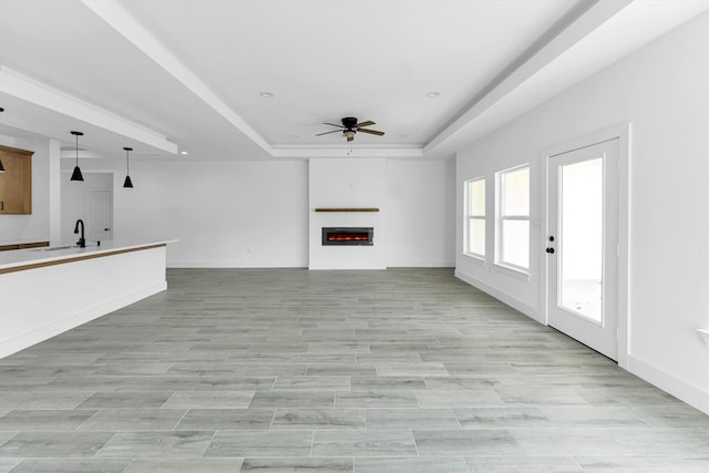 unfurnished living room with light wood-type flooring, ceiling fan, sink, and a tray ceiling