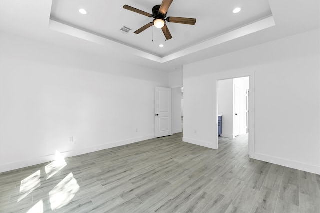 empty room featuring ceiling fan, a tray ceiling, and light hardwood / wood-style floors