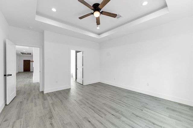 empty room with light wood-type flooring, a tray ceiling, and ceiling fan