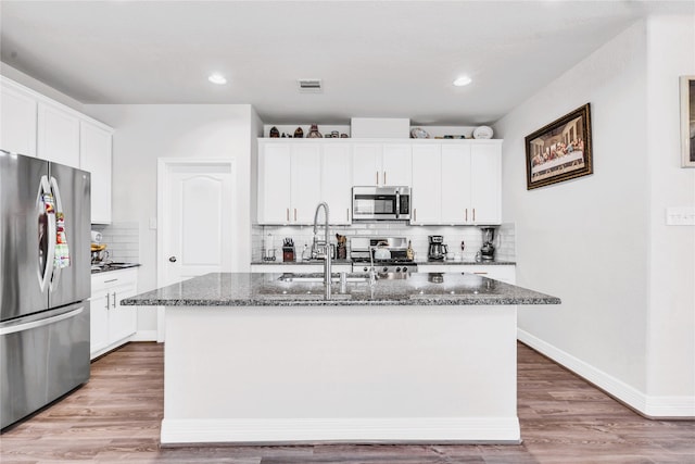 kitchen featuring a center island with sink, white cabinetry, dark stone counters, and appliances with stainless steel finishes