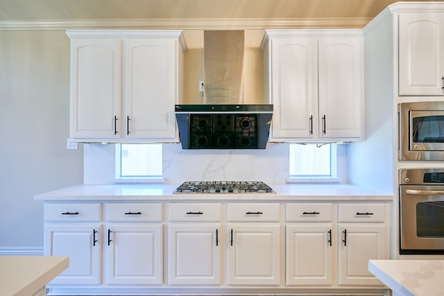 kitchen featuring wall chimney exhaust hood, backsplash, ornamental molding, white cabinetry, and appliances with stainless steel finishes