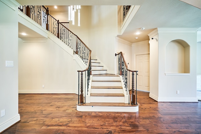 staircase with ornamental molding, hardwood / wood-style floors, a textured ceiling, and a towering ceiling