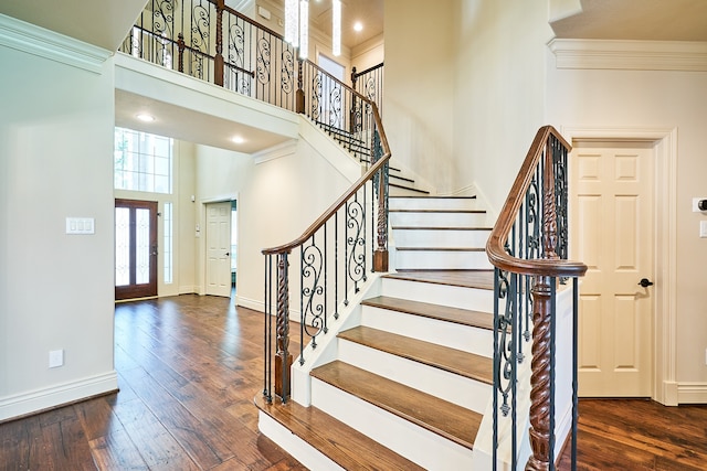 stairway with crown molding, a towering ceiling, and wood-type flooring